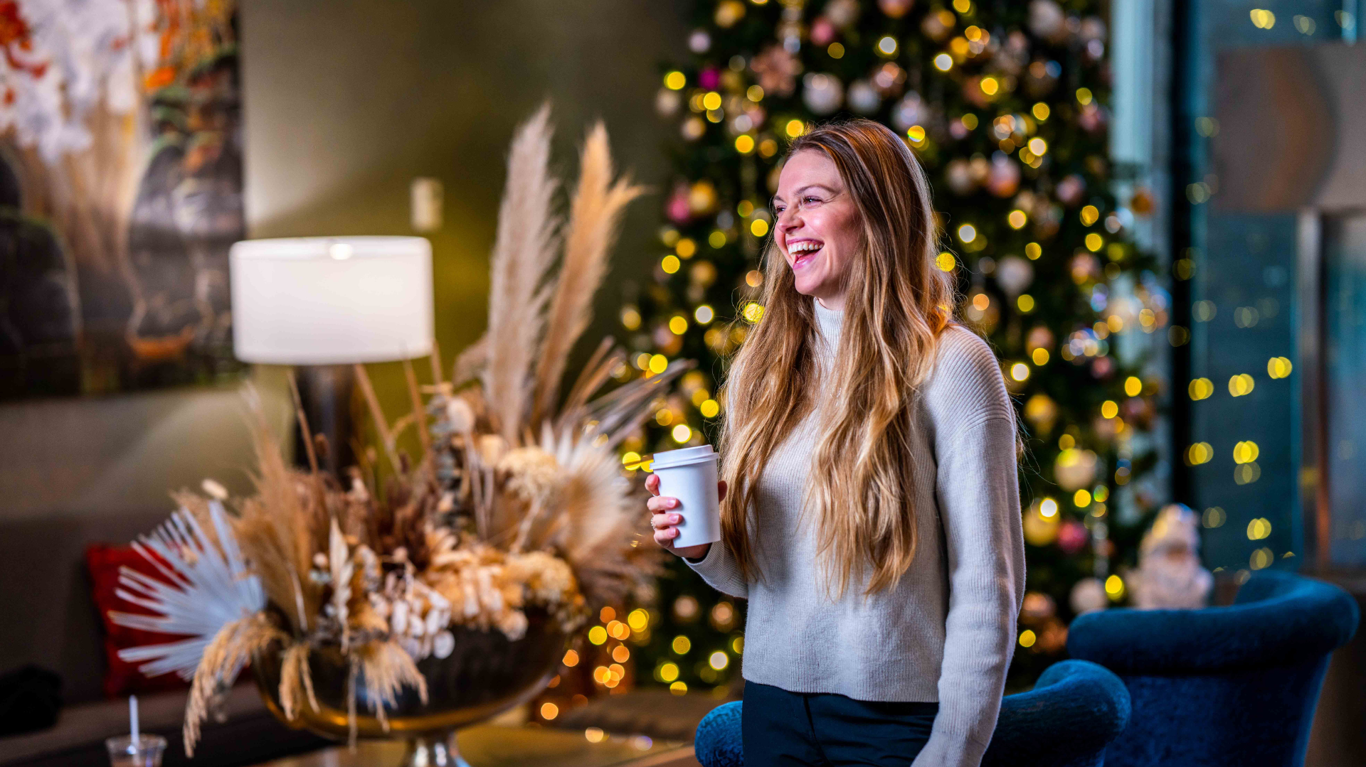 A Person Sitting In Front Of A Christmas Tree Holding A Cup